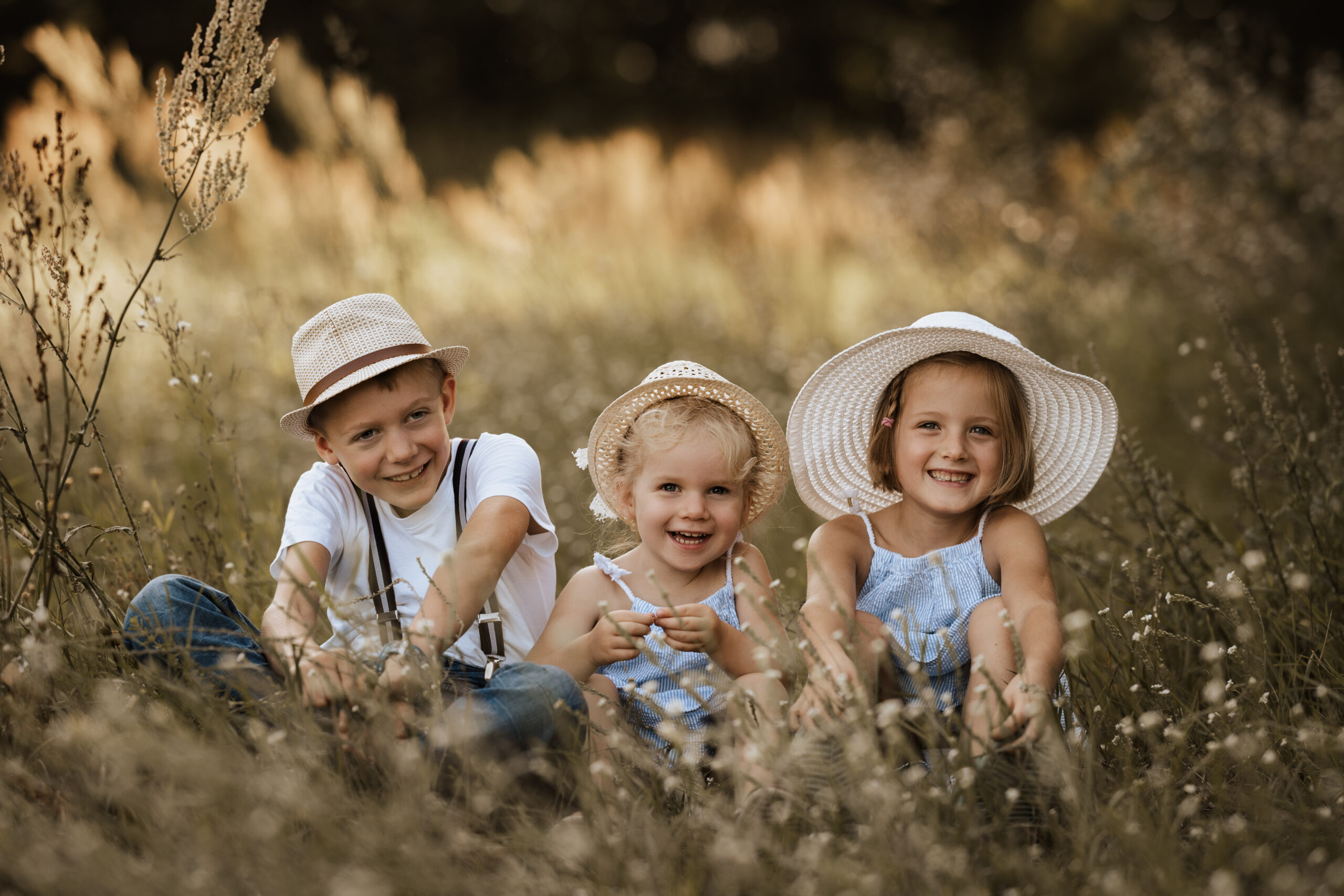 Lachende Kinder mit Strohhüten in sommerlicher Wiese.