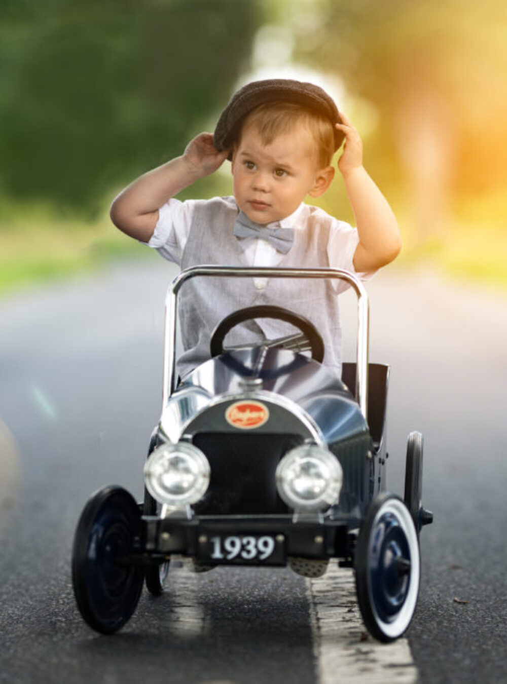 Kleiner Junge mit Anzug sitzt im Oldtimer Spielzeugauto.